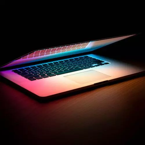 Mac laptop, glowing, partially closed, dark background.
